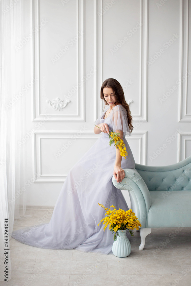The girl looks down and touches the flower on her shoulder restoration of antique furniture, interior design. a room with white plaster mouldings,a blue sofa upholstered in a blue velvet carriage tie. The girl looks down and touches the flower on her shoulder restoration of antique furniture, interior design. a room with white plaster mouldings,a blue sofa upholstered in a blue velvet carriage tie.