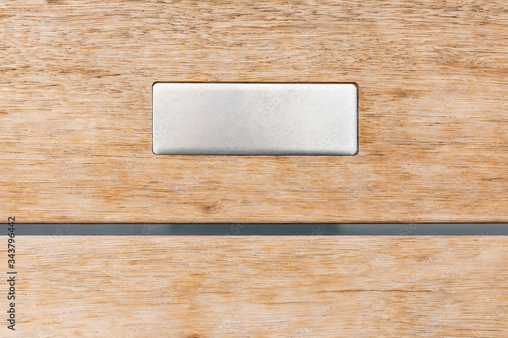 Detail of a metal name plate in the middle with an empty space on a light colored wooden background