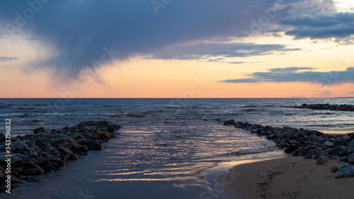Fototapeta Naklejka Na Ścianę i Meble -  Sunset on a sandy beach. Dramatic sky. Stone pier.