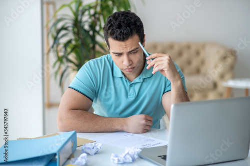 Upset dark-haired male sitting at his desk, filling in unemployment claim