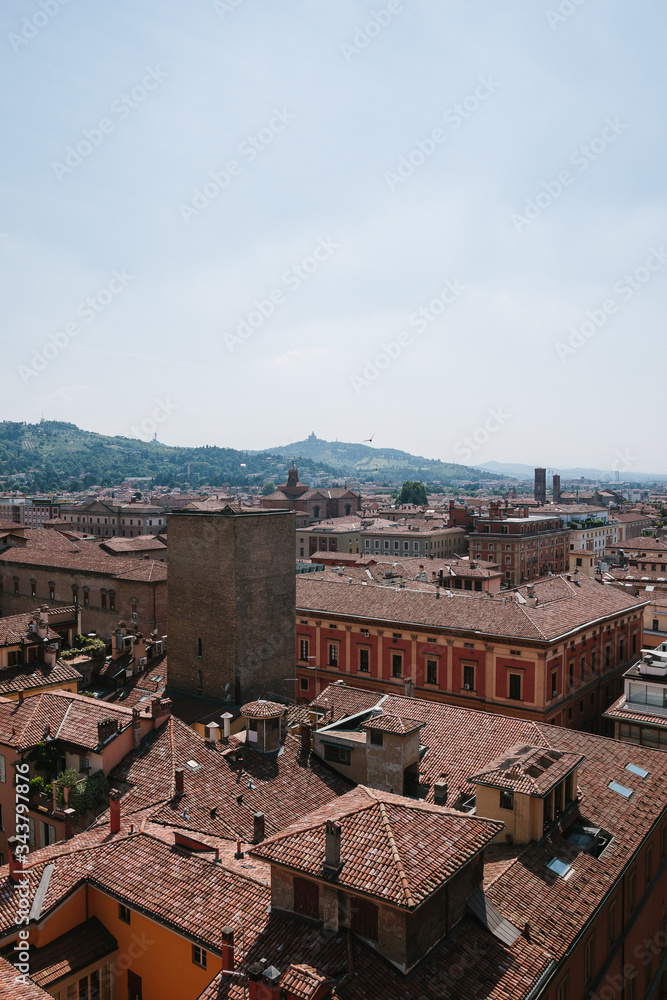 Italian top view in tuscany. Roof tile and in sunny day in Bologna. Old Europe. Scenery in summertime. Tower in the center of the city and mountains on background. Nobody. Vertical shot of cityscape.