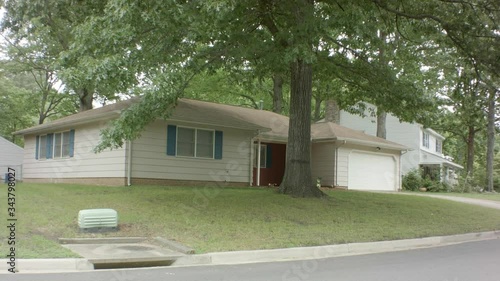 Street view of a white suburban house with blue shutters.  Big tree out front. photo