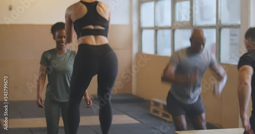 Two fit young women in sportswear smiling and
doing box jumps together during an exercise class
in a gym
 photo