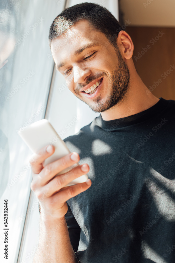 low angle view of happy man using smartphone near window at home low angle view of happy man using smartphone near window at home