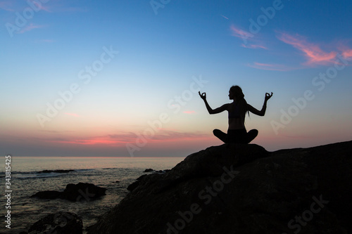 Silhouette of yoga woman on the ocean beach in the amazing twilight.