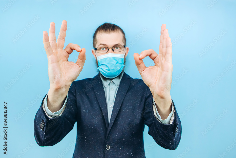 a successful muschin in a suit, glasses and a medical mask on a blue background. Businessman. A private entrepreneur affected by the coronavirus epidemic. Pandemic covid 2019. a successful muschin in a suit, glasses and a medical mask on a blue background. Businessman. A private entrepreneur affected by the coronavirus epidemic. Pandemic covid 2019.