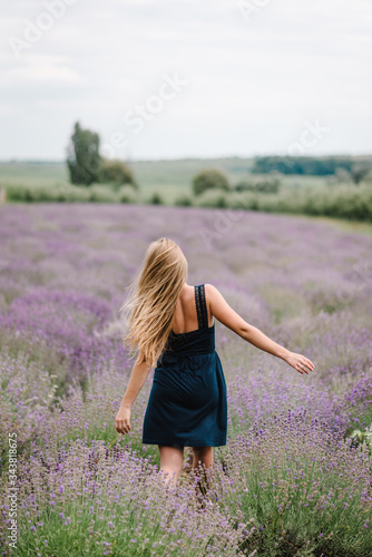 Beautiful girl in dress running and flying long hair on purple lavender field. Beautiful woman walk on the lavender field on sunset. Enjoy the floral glade, summer nature. Hairstyle. Back view.