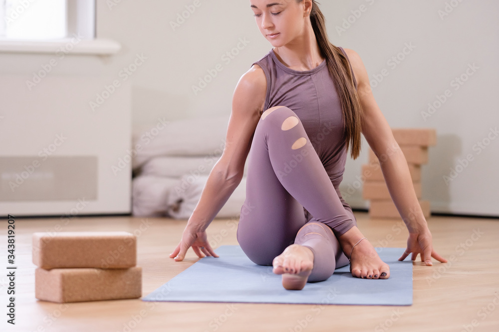 Fototapeta premium Athletic and healthy young caucasian girl in a purple suit doing fitness on blue mat in the cozy living room floor. Quarantine yoga and pilates sports concept. Copyspace