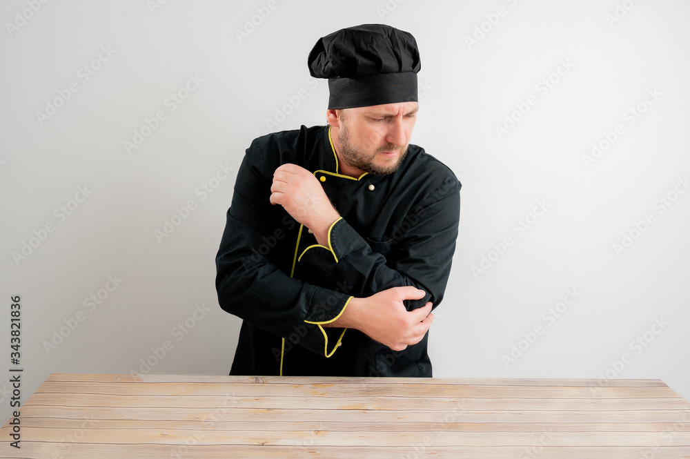 Fototapeta premium Young male chef in black uniform has elbow pain