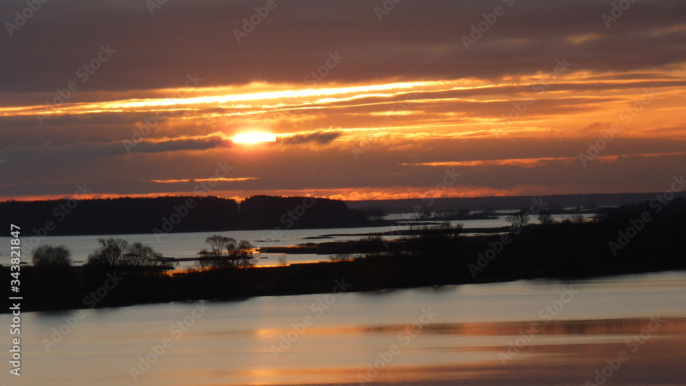 Water expanses with a frosted surface from ripples with glimpses of reflected orange hot sky.On the horizon, the sun falling into the clouds, the silhouette of the Islands in the twilight at sunset