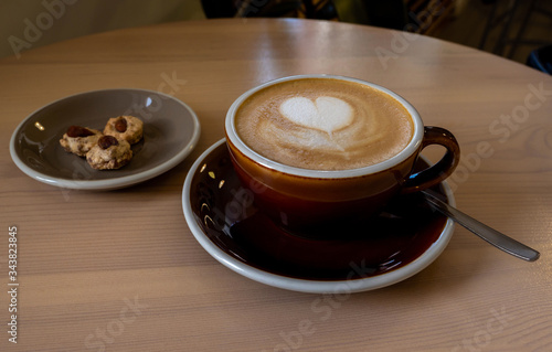 a dark Cup of coffee and marshmallows and a plate of cookies is placed on a wooden table. drawing of a heart on foam. love.. close up.