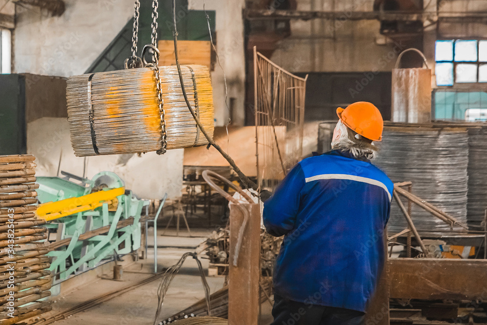 Fototapeta premium A working man in a reinforcement workshop controls equipment for moving metal structures