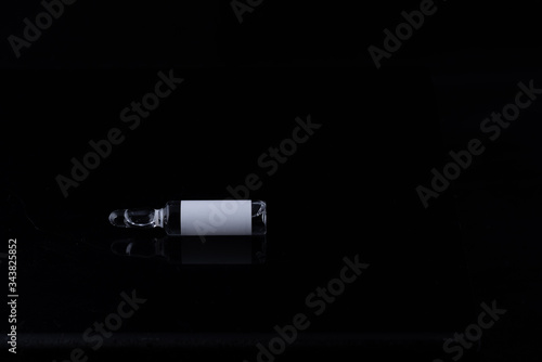 Ampoule with liquid inside, without the inscription on a label on a black background.