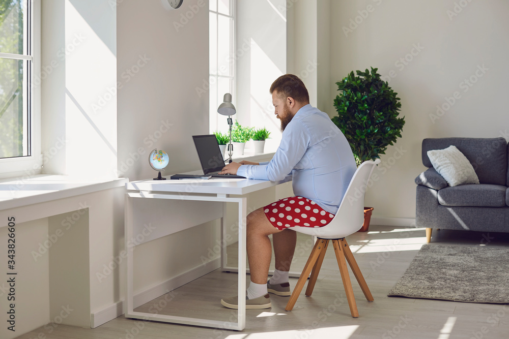 Online work at home. Funny fat businessman in red shorts works communicates using laptop at home. Online work at home. Funny fat businessman in red shorts works communicates using laptop at home.