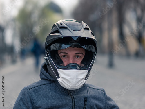 portrait of a man in a helmet. on a motorcycle helmet a white medical mask. photo on the street against the background of houses. coronavirus, disease, infection, quarantine, covid-19