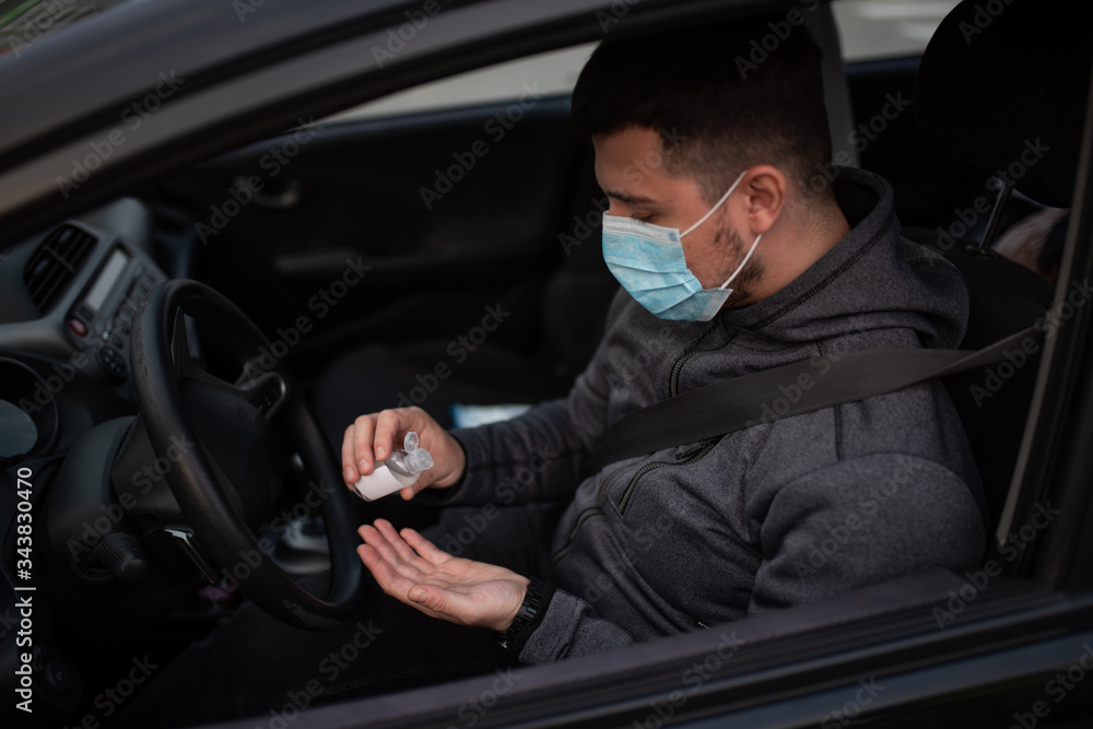 A man use an antiseptic gel into his hands while sitting in a car. A man in a medical mask to protect viruses. masked man in a car. coronavirus, disease, infection, quarantine, covid-19 A man use an antiseptic gel into his hands while sitting in a car. A man in a medical mask to protect viruses. masked man in a car. coronavirus, disease, infection, quarantine, covid-19