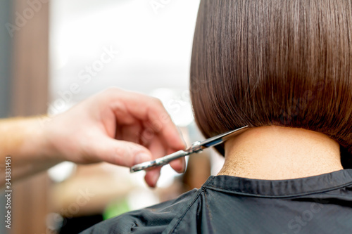 Back view of hairdresser hand is cutting hair tips of woman short hairstyle in hair salon. photo