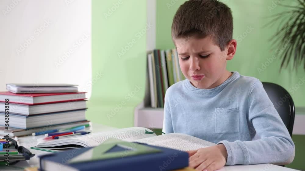 home education, upset tired child does homework, reads a book and props his forehead with his hand while sitting at a table with school supplies, hard learning home education, upset tired child does homework, reads a book and props his forehead with his hand while sitting at a table with school supplies, hard learning