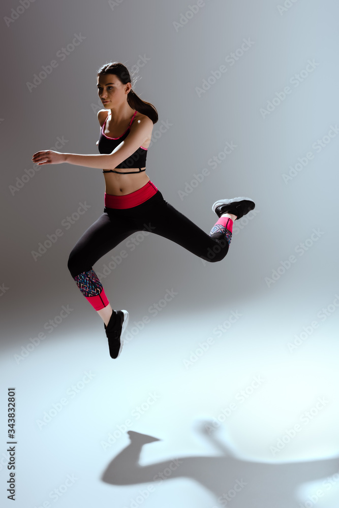 attractive girl in sportswear jumping on grey