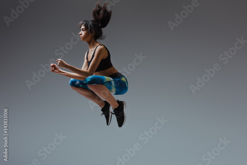 sportive african american girl in sportswear jumping on grey
