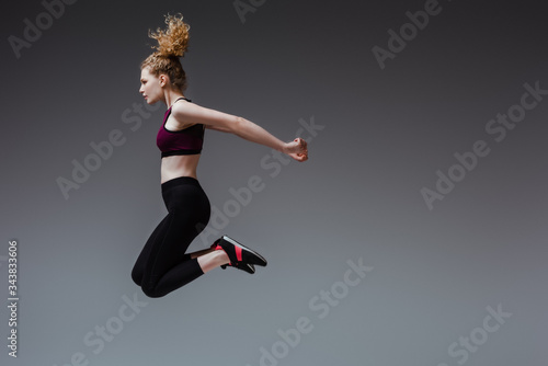 Fototapeta Naklejka Na Ścianę i Meble -  profile of curly woman in sportswear jumping on grey