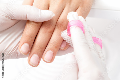 Close-up of manicurist hands is removing dust from nails with a brush to cleaning nails in manicure salon.