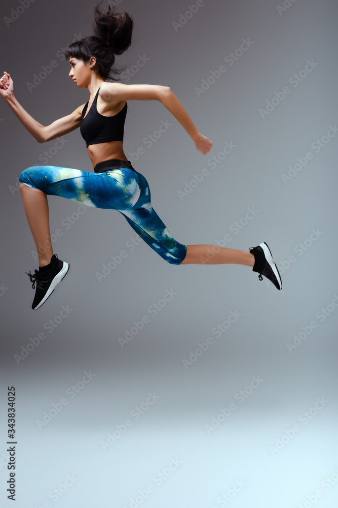 side view of african american girl in sportswear jumping on grey