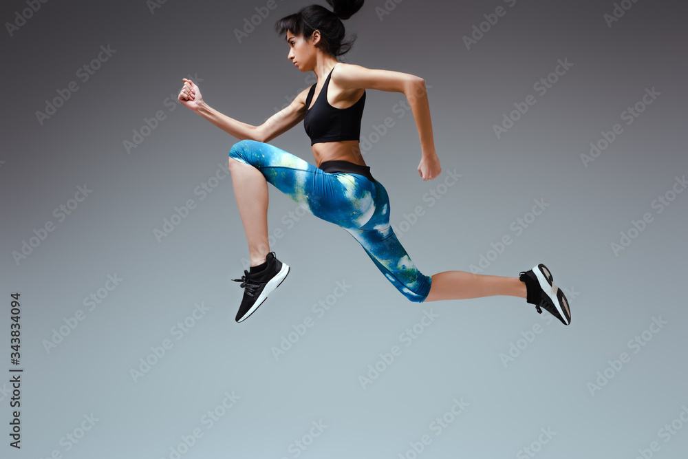 side view of african american woman in sportswear jumping on grey