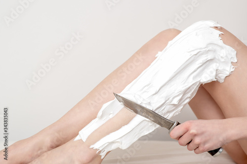 Woman hand is shaving her leg by knife with shaving foam on white background.