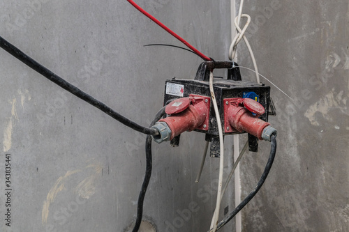 Chaotischer Stromverteiler mit Kabel und roten Steckern in einem Rohbau.