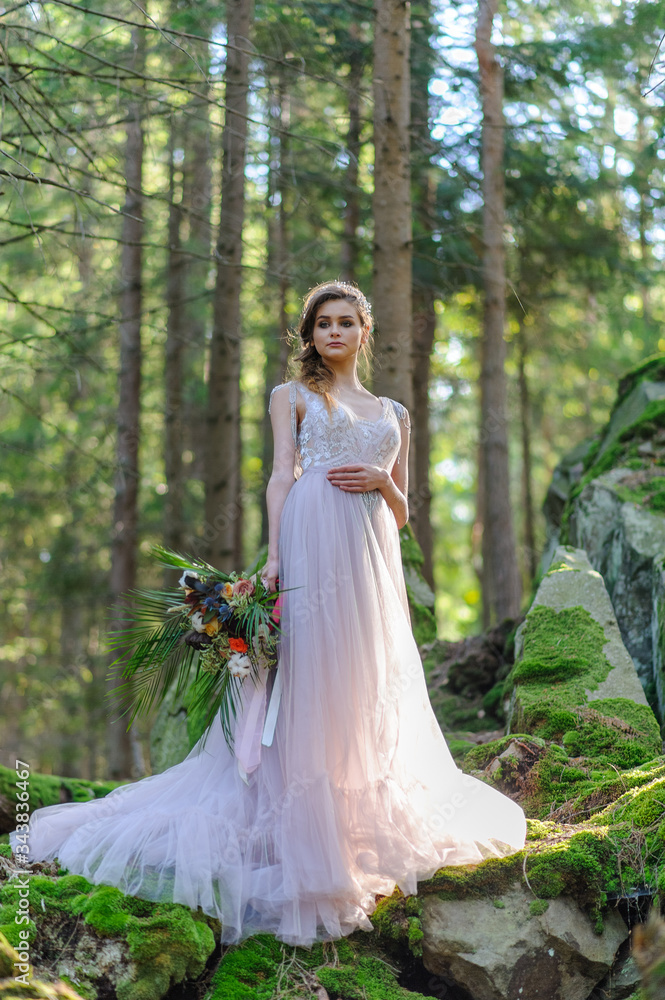 Happy bride in a pink wedding dress. The girl holds a wedding bouquet in her hands. Boho style wedding ceremony in the forest.
