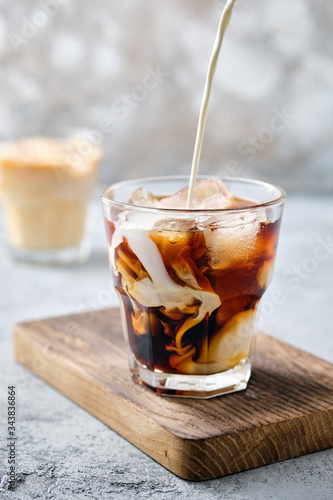 Pouring cream in iced coffee in rocks glass