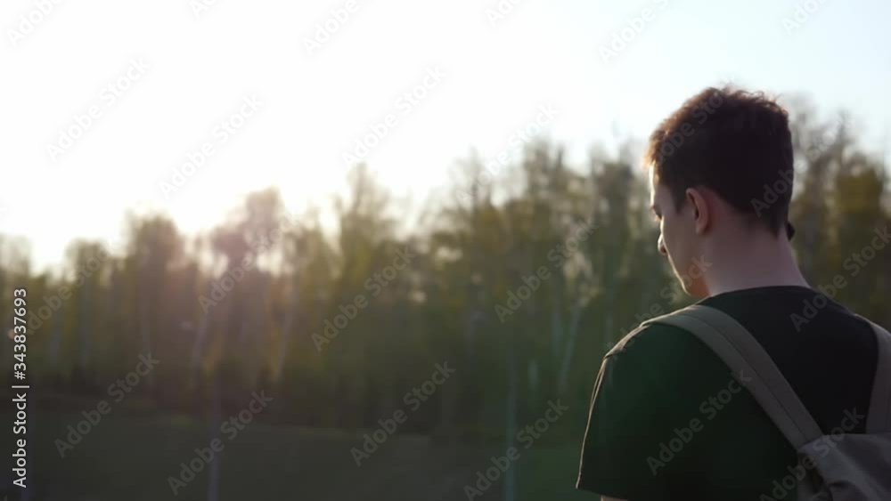 The traveler looks at the road and enjoys the soft rays of the sun, travels abroad, stands on the bridge. A man with a tourist backpack at sunset. The traveler looks at the road and enjoys the soft rays of the sun, travels abroad, stands on the bridge. A man with a tourist backpack at sunset.
