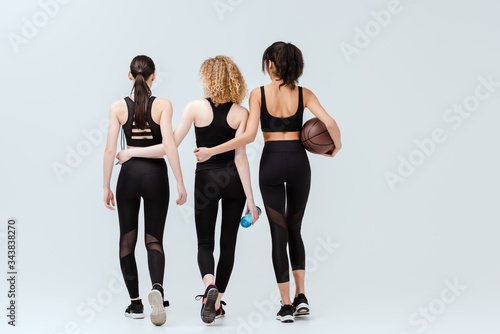 back view of multicultural girls walking with sport equipment on white