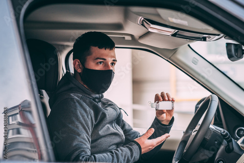 man in a black medical mask. handsome brunette driving an expensive car. antiseptic gel disinfects hands. thief, steal, coronavirus, disease, infection, quarantine, medical mask, covid-19 © Evghenii Blanaru