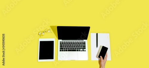 Hand using gadgets, devices on top view, blank screen with copyspace, minimalistic style. Technologies, modern, marketing. Negative space for ad, flyer. Yellow color on background. Stylish, trendy.