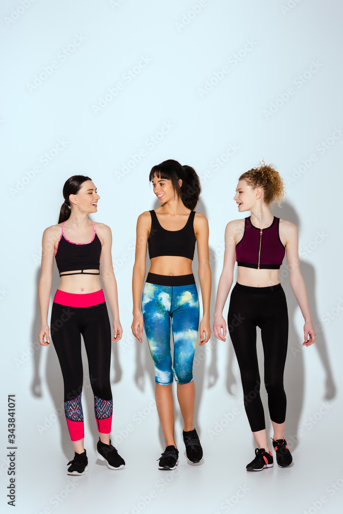 Obraz premium multicultural and happy women in sportswear walking on white