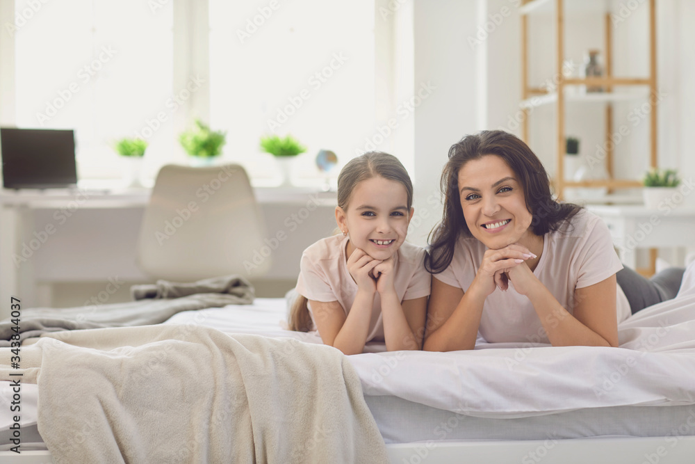Happy mother's day. Mother and daughter smiling lying looking at the camera on the bed in the room. Happy mother's day. Mother and daughter smiling lying looking at the camera on the bed in the room.