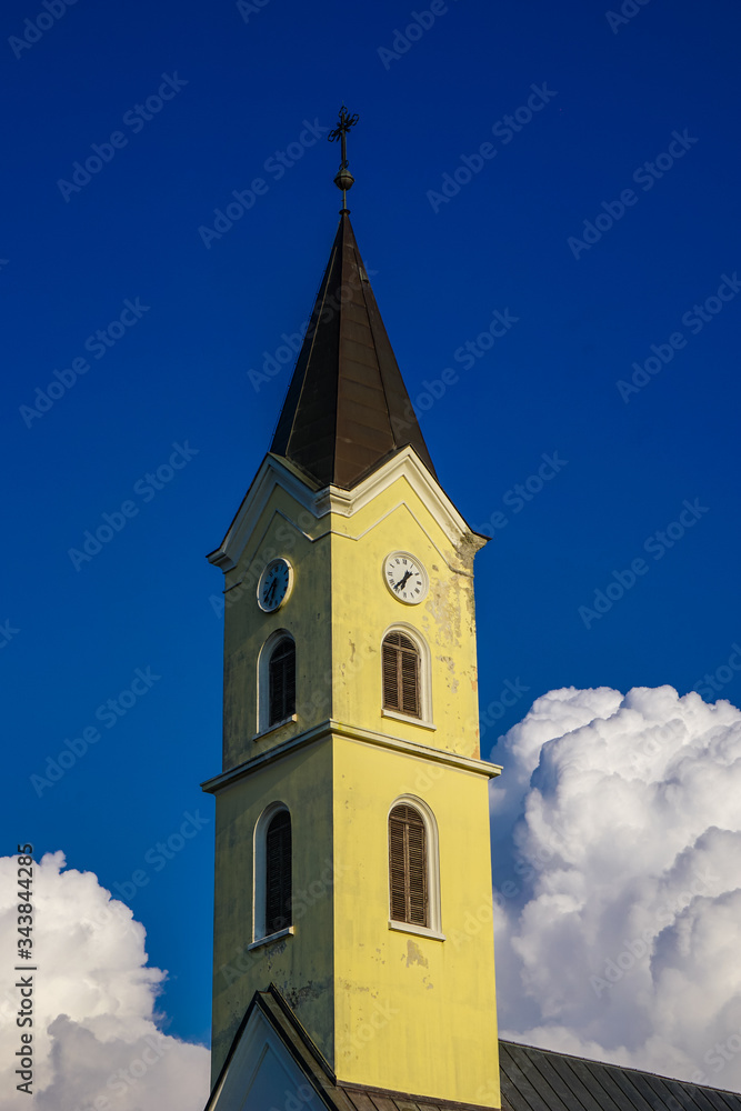 Yellow tower of a catholic temple on a background of blue sky and white clouds