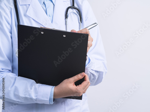 Doctor with stethoscope in white coat holding clipboard, writing medical record diagnosis, isolated on white background, close up, cropped view.