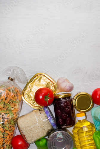 Different food on wooden background with copyspace - pasta, fresh vegatables and semi-finished products in jars. Delivery food, donation concept, vertical composition