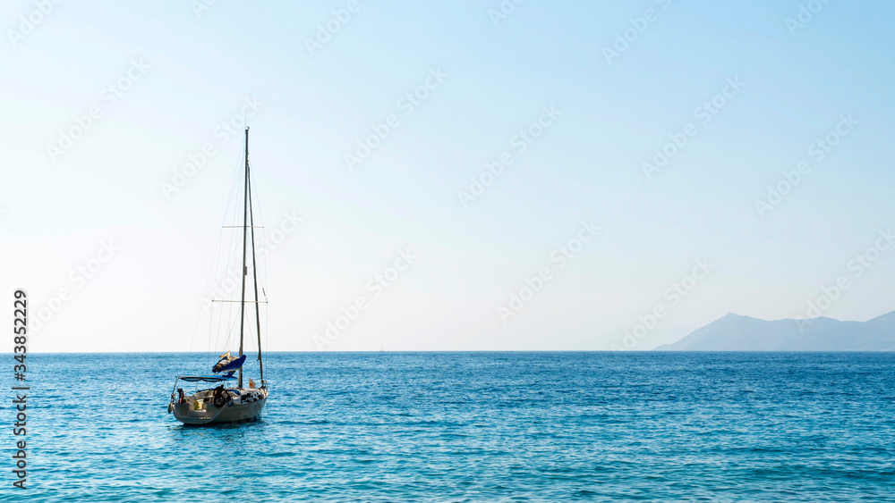 Single white sailing boat traveling in the blue Aegean sea with island and sky background and with copy space.

