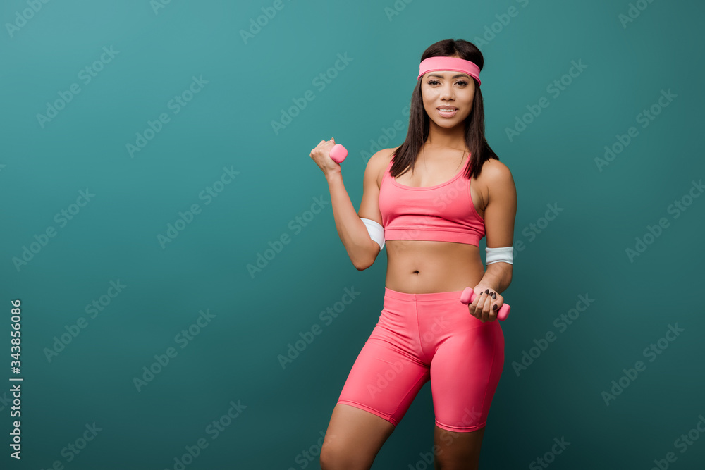 African american sportswoman smiling and training with dumbbells isolated on green African american sportswoman smiling and training with dumbbells isolated on green