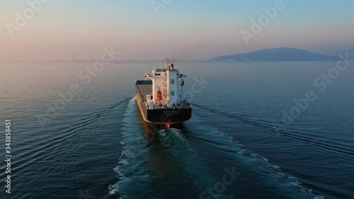 Aerial view following the ultra large cargo ship at sea leaves port at sunset