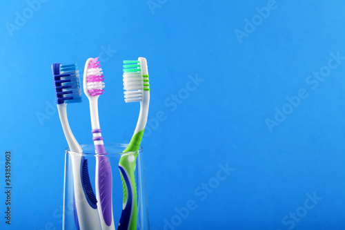 Three toothbrushes in a glass cup on a blue background  place for your text