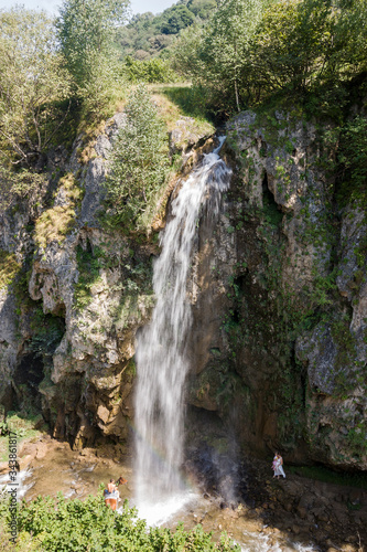 A rapid mountain stream of water forms a large waterfall. The stream of water rushes from the mountain height into the valley. 