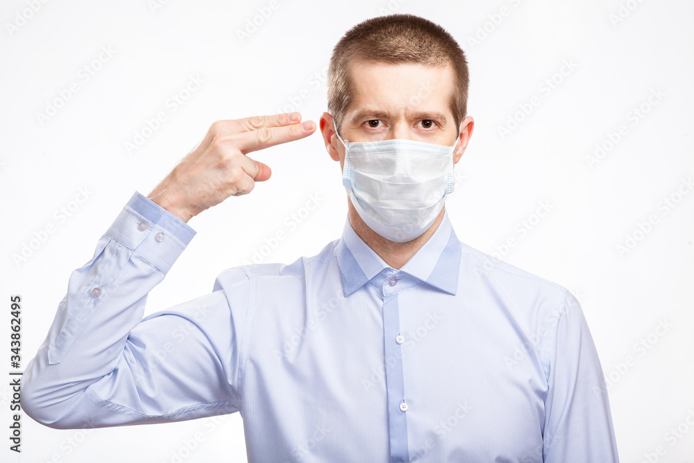 A handsome young man in a medical mask, a blue light shirt shows his finger on his head, in full-face, staring at the camera . Isolated A handsome young man in a medical mask, a blue light shirt shows his finger on his head, in full-face, staring at the camera . Isolated