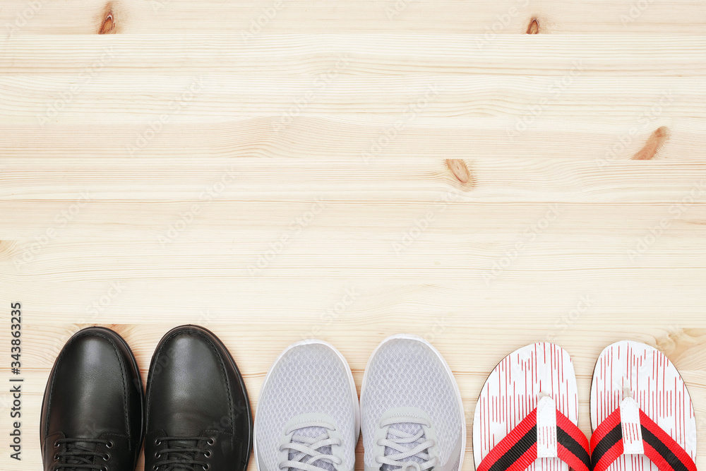 top view of black leather shoes, sneakers and beach slippers on wooden background top view of black leather shoes, sneakers and beach slippers on wooden background