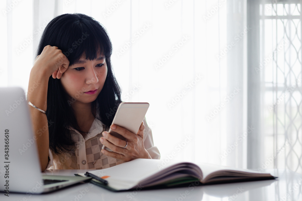 Asian woman using smartphone with computer laptop and working at home for business, self-quarantine, staying home and social distancing in coronavirus or Covid-2019 outbreak situation concept Asian woman using smartphone with computer laptop and working at home for business, self-quarantine, staying home and social distancing in coronavirus or Covid-2019 outbreak situation concept