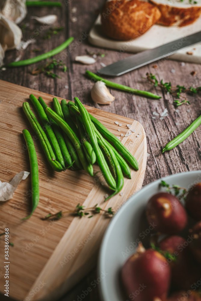 Close-up of green prepared fine beans on a rustic table with red potatoes with garlic and rosemary Vertical
Close-up of green prepared fine beans on a rustic table with red potatoes with garlic and rosemary Vertical